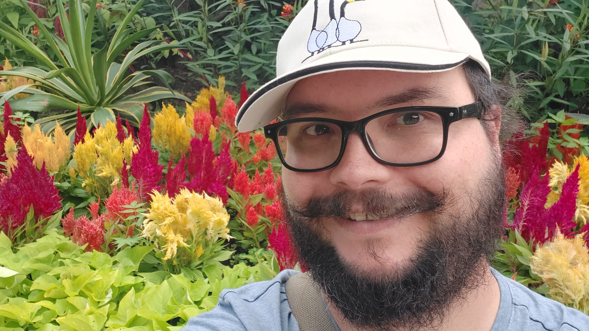 A man short hair and bushy facial hair sits in front of yellow and red flowers